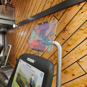 Close-up of a treadmill display showing a welcome screen and the Slim-Grip® Ultra Pro Universal Tablet Holder with Clamp Mount in a gym with wooden paneled walls. Other equipment and a balcony are visible in the background.