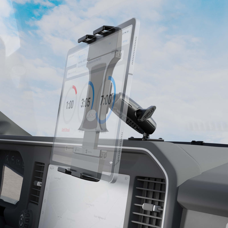 A Slim-Grip® Ultra Pro Universal Tablet Holder with Aluminum Drill-Base Mount secures a tablet on a vehicle dashboard, showing a timing app with circular timers; the windshield and cloudy sky are visible in the background.
