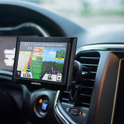 A Garmin GPS device is securely attached in a car with the Car Vent Mount, displaying driving directions for the New Jersey Turnpike, including lane guidance, speed limits, and current speed. The dashboard and part of the steering wheel are also visible.
