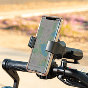 A RoadVise® Ultra Motorcycle Handlebar Mirror Pinch Bolt Stem Phone and Tablet Mount in black secures a smartphone displaying a map to a bicycle handlebar. The blurred background features trees and a pathway outdoors.