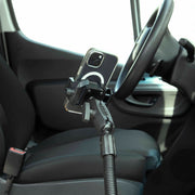 A smartphone is secured in the RoadVise® Ultra Holder with Heavy-Duty Seat Rail Mount, installed inside a modern car next to the driver’s seat and steering wheel, with a visible seatbelt buckle in the interior.