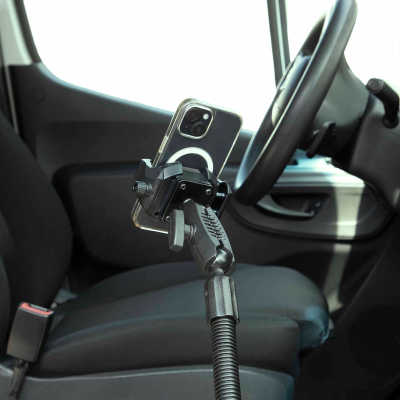 A smartphone is secured in the RoadVise® Ultra Holder with Heavy-Duty Seat Rail Mount, installed inside a modern car next to the driver’s seat and steering wheel, with a visible seatbelt buckle in the interior.