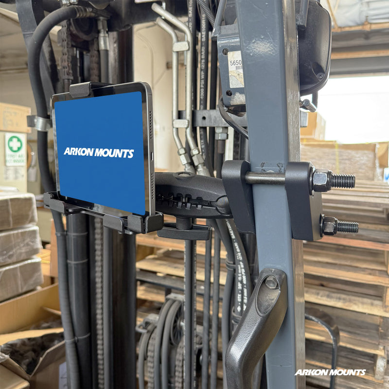 A tablet, securely mounted on a forklift using the XMS™ Heavy Duty Forklift Mount with LockVise™ Metal XL Locking Tablet Holder from Arkon Mounts, sits in a busy warehouse surrounded by boxes and equipment.