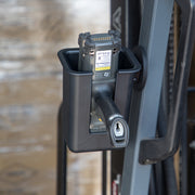 An Arkon Mounts Magnetic Mount Device & Barcode Scanner Holder in black is attached to a gray metal frame, securely holding a handheld barcode scanner, with a pallet partially visible in the blurred background.
