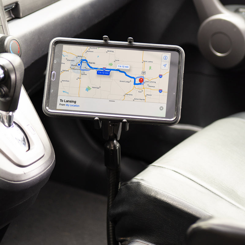 A Slim-Grip® Ultra Phone Seat Rail or Floor Car Truck Mount holds a smartphone displaying navigation to Lansing, securely positioned by the drivers seat and gear shift for easy access.
