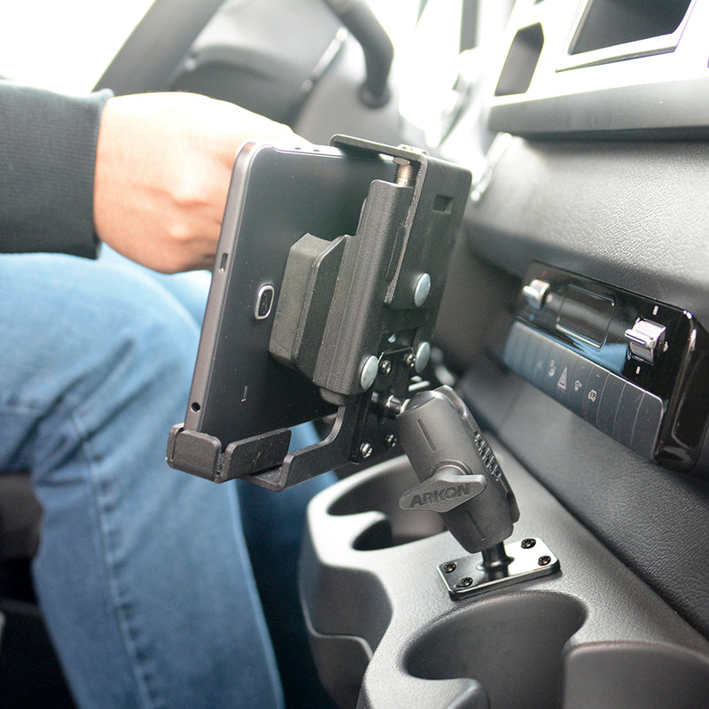 A person adjusts a smartphone mounted in the LockVise™ Metal Locking Tablet Mount with Drill Base Mount attached to a car’s dashboard near the cup holders, with the interior visible.