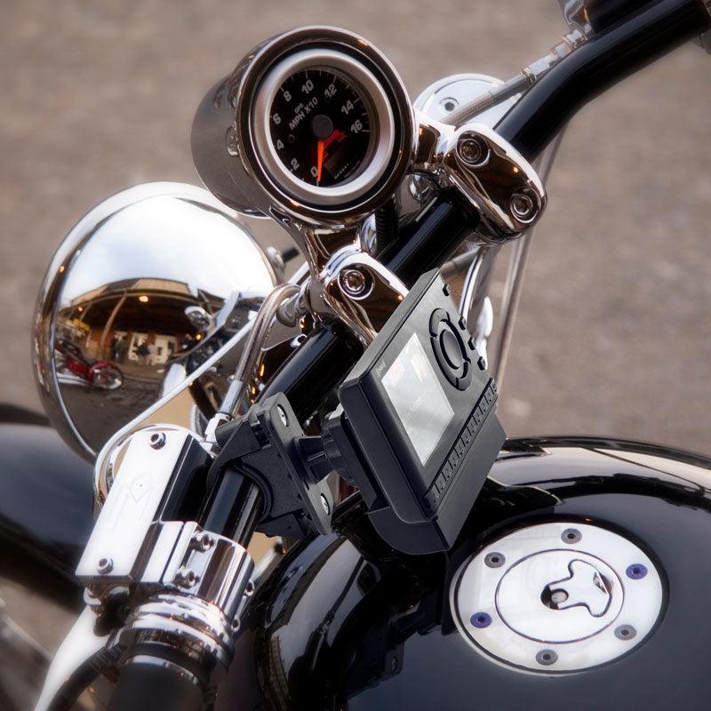 Close-up of a motorcycle handlebar with a speedometer, chrome finish, and a Bike or Motorcycle Handlebar Mount for XM and Sirius Satellite Radio (4-Hole AMPS pattern) securing a digital device. Building reflections appear in the metal surfaces.