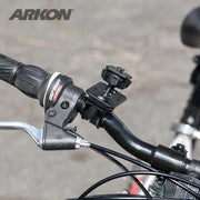Close-up of a bicycle handlebar with a gear shifter, brake lever, and a Bike or Motorcycle Handlebar Mount for XM Satellite Radio (compatible with Bracketron, Scosche). Blurred pavement in the background.