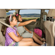 Two young girls sit in the backseat, smiling and watching a screen held by the Center Extension Car Headrest Slim-Grip® Tablet Mount for iPad, Note, and more. One points at the display while both look relaxed and entertained. A pink backpack sits beside them.