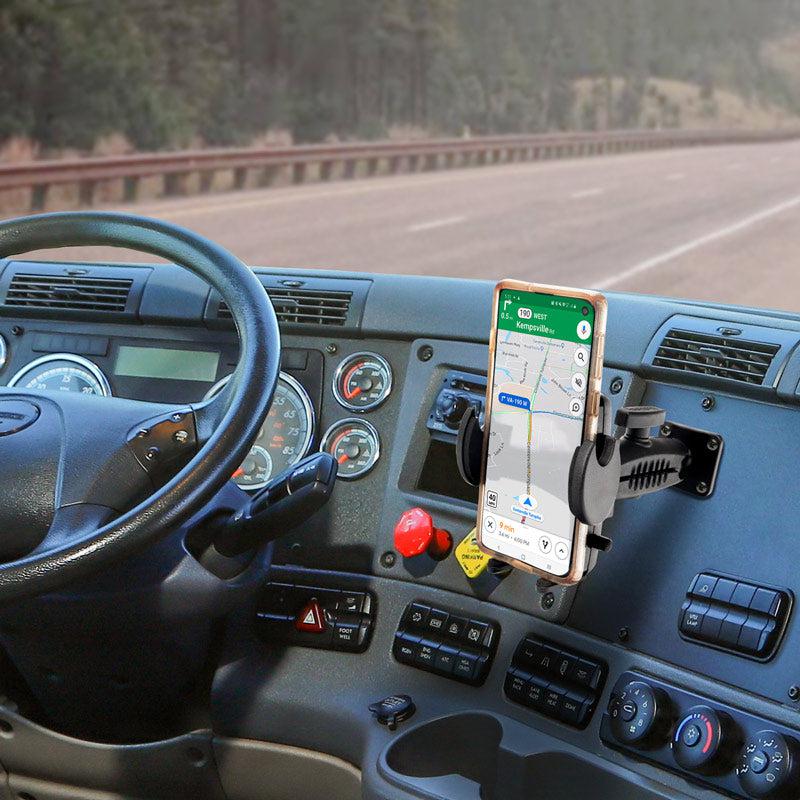 A Drill-Base Mega Grip™ Phone Mount secures a smartphone with navigation on a truck dashboard; the adjustable arm holds the phone near the steering wheel and control panel, with a highway scene visible through the windshield.