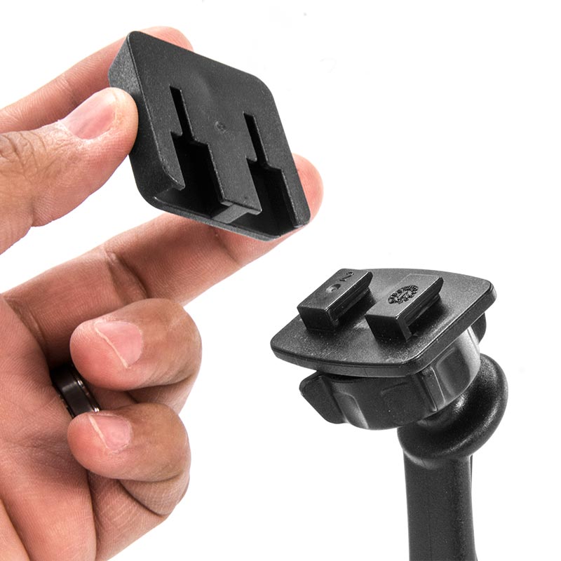A hand holds a rectangular black Dual-T Mount Adapter for XM Radio, Scosche, or Bracketron Single-T Holders above a matching mounting base, both featuring interlocking slots that suggest assembly or attachment.