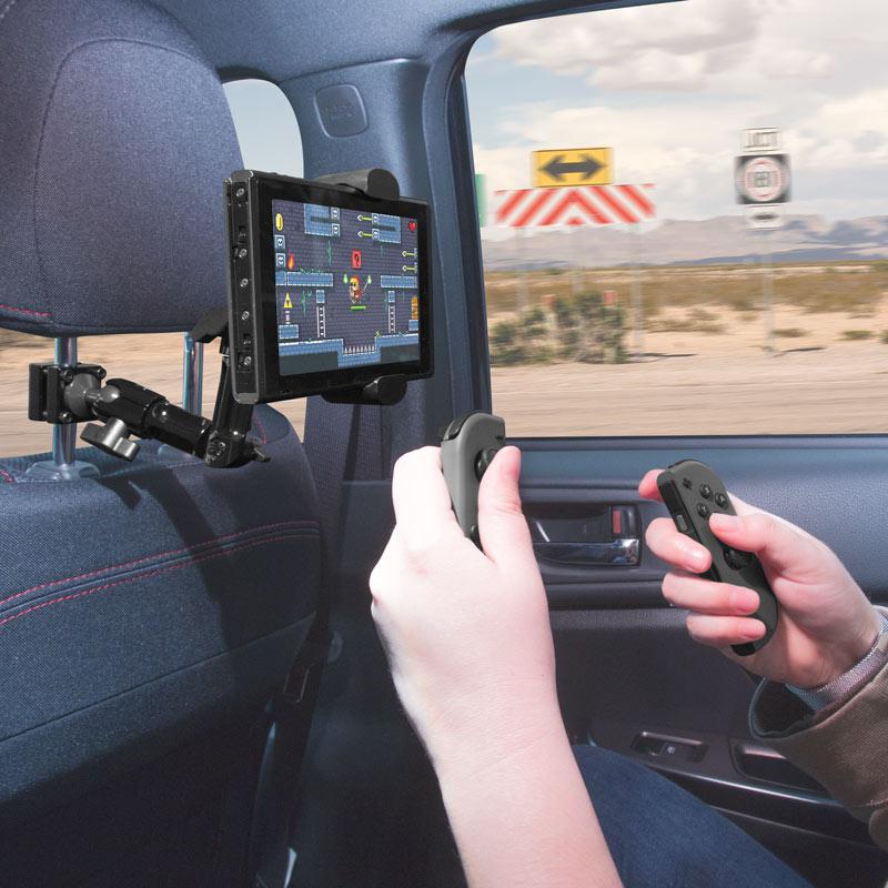 Two passengers use a Heavy-Duty Multi-Angle Headrest Mount to play video games with wireless controllers on a road trip, enjoying rear seat entertainment as desert scenery passes by outside the car window.