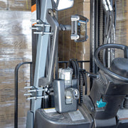 Close-up of a forklift’s control area showcasing the Large Barcode Holster Forklift Front Guard Mount with 5 Shaft and control levers, with stacked cardboard boxes in the background highlighting advanced forklift technology.