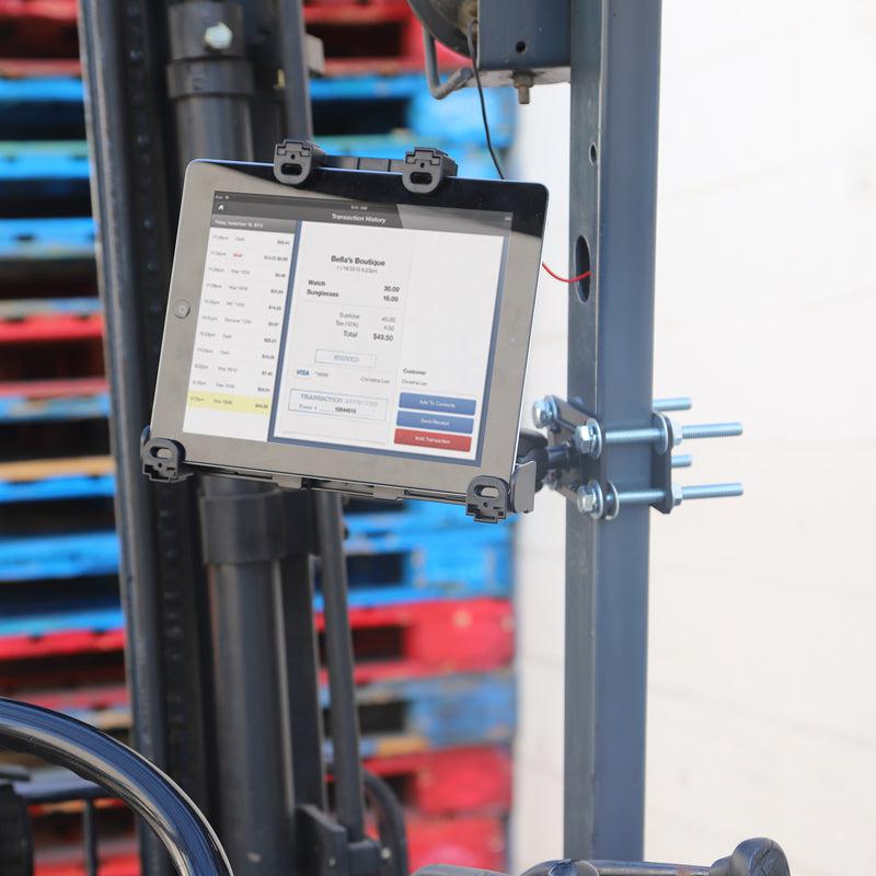 A LockVise™ Locking Forklift Front Guard Tablet Mount with 5 Robust™ Shaft secures a tablet to industrial equipment running inventory software, with colorful stacked pallets in the background of this dynamic warehouse scene.