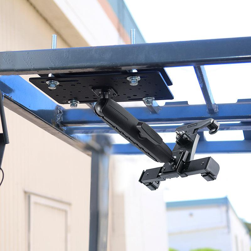 A close-up of the LockVise™ Locking Forklift Overhead Guard Tablet Mount with 8.5 Metal Shaft, in black, attached to a blue metal frame outdoors with buildings softly blurred in the background.