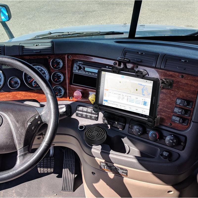 A LockVise™ Locking Tablet Mount with Multi-Angle Arm holds a tablet showing map and route info on a truck dashboard, surrounded by gauges and controls as sunlight shines through the windshield onto the steering wheel and dash.