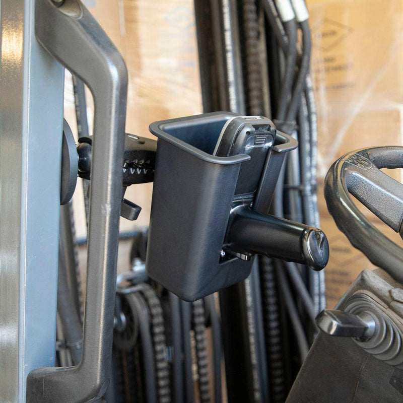 A Magnetic Mount with Barcode Scanner Holster Holder is attached to industrial equipment near the steering wheel, securely holding a smartphone upright, with machinery and a cardboard box in the background.