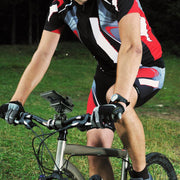 A cyclist in red, black, and white rides on grass, gripping the handlebars and wearing gloves. A Mega Grip™ Phone Holder with Clamp Mount is attached to the bike, securing a device. The upper part of the rider’s head is not visible.