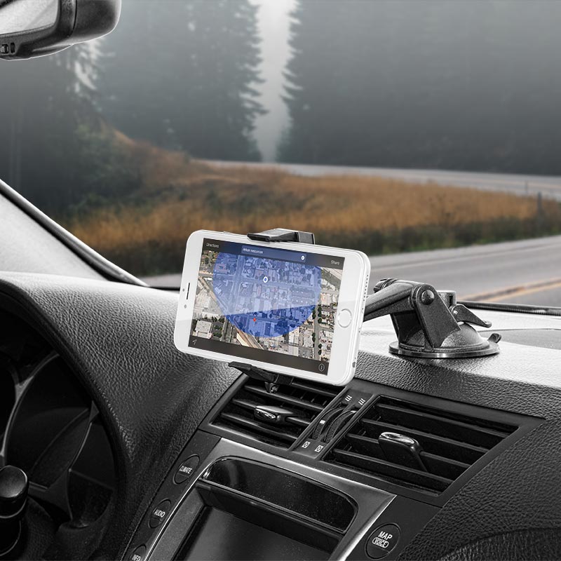 A smartphone shows a map while secured in the Mobile Grip 2 Phone Car Mount with Sticky Suction on the dashboard. The car is parked by the road, and trees along with a foggy forest are seen through the windshield.
