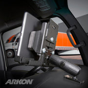 A LockVise™ Metal Locking Tablet Mount with Drill Base and Magnetic Micro USB Charge Cable for Commercial and Enterprise secures a tablet to a vehicle’s dashboard, with a semi-truck outside. The ARKON logo appears in the bottom left corner.