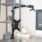 The Remarkable Creator™ Pro+Plus with Clamp Mount, in black, is attached to a glass desk next to a monitor, surrounded by a candle and stacked books, with vintage cameras displayed on a shelf in the background.