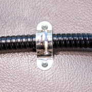 The Replacement Metal Conduit for Seat Rail Mounts is secured to a textured brown surface with a metal clamp and two screws, providing vibration prevention similar to a floor mount gooseneck.