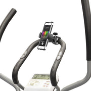 Close-up of an exercise bike handlebar with the RoadVise® Phone Clamp Post Mount holding a smartphone that displays a colorful graph. The bike’s digital screen shows workout stats like time, distance, and calories burned.