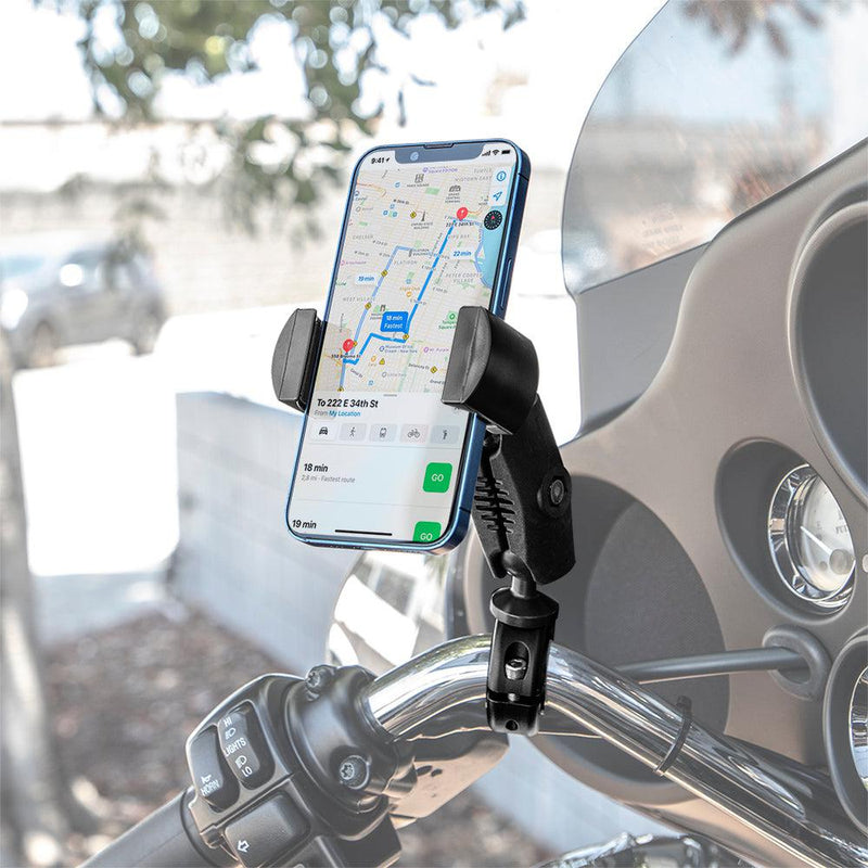 A RoadVise® Phone Holder with Aluminum Handlebar Mount and 2.75 Shaft secures a smartphone displaying a navigation map on a motorcycle handlebar, with an outdoor background featuring a blurred wall and trees.
