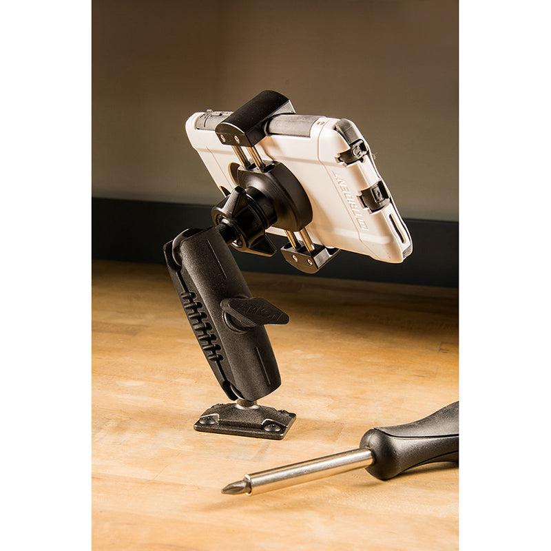 A white smartphone is secured horizontally in the RoadVise® Phone Holder with Drill Base and Adjustable Arm, attached to a wooden surface. A screwdriver lies beside the mount.