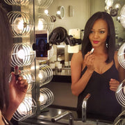 A woman in a black top applies lipstick while looking in a well-lit mirror, her phone filming her reflection using the RoadVise® Phone Holder with Sticky Suction Mount and Shaft.