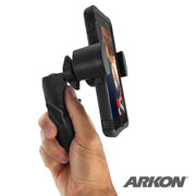 A hand holds a smartphone mounted on the black RoadVise® Phone Tripod Mount. The screen shows a blurred image, with the ARKON logo in the bottom right corner—perfect for live streaming on the go.
