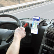 A person drives with their left hand on the wheel, using a GPS navigation app on their smartphone, which is secured by the RoadVise® Phone Holder with Adhesive Car or Truck Mount. The road is visible through the windshield.