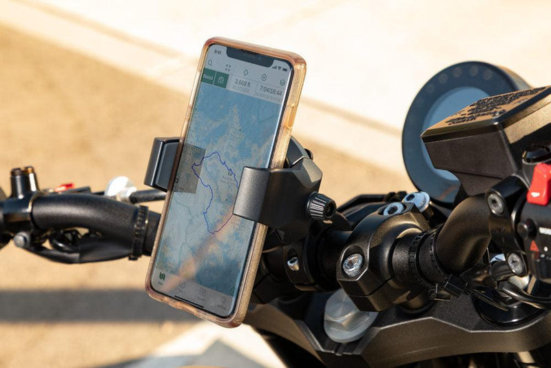 A smartphone with a map is held by the RoadVise® Ultra Holder with Aluminum Handlebar Mount on motorcycle handlebars for safe navigation. The photo is taken outdoors in daylight.