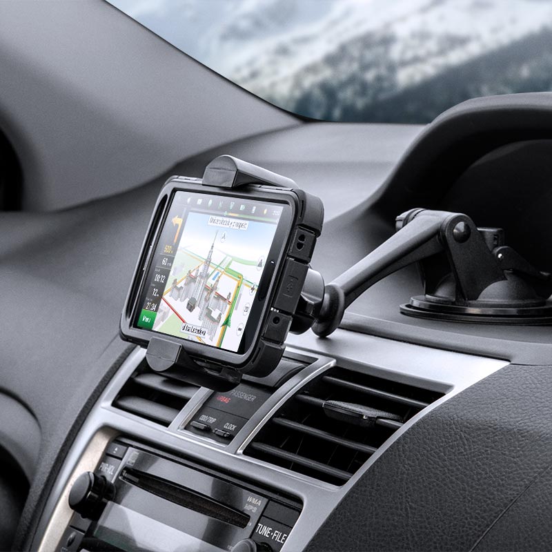 The RoadVise® XL Car Dash or Windshield Mount is attached above the air vents, securely holding a GPS device with navigation directions visible. A blurred winter scene is seen through the windshield.