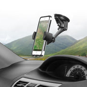 A smartphone displaying a map is secured to the car dashboard with the RoadVise® XL Car Dash or Windshield Mount, while green hills and a cloudy sky are visible through the windshield.