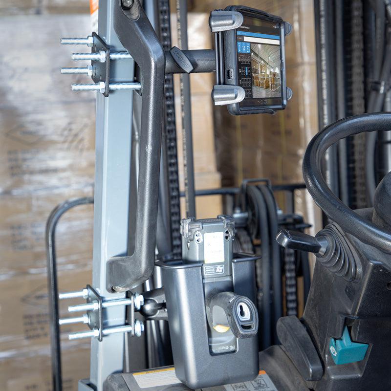 A close-up shows a Slim-Grip® Tablet Holder with Forklift Front Guard Mount and 3.75 Shaft securely attached to the forklift’s frame, with dashboard controls and part of the steering wheel also visible.