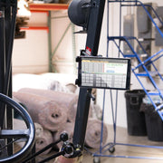 A close-up of a forklift control area shows the Slim-Grip® Tablet Holder with Forklift Front Guard Mount and 3.75 Shaft displaying software; rolls of carpet and warehouse shelves appear in the background.