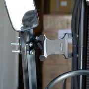 Close-up of the Slim-Grip® Tablet Holder with Forklift Front Guard Mount and 3.75 Shaft, securely attached to a metal bar near a rectangular mirror, with blurred cardboard boxes in the warehouse background.