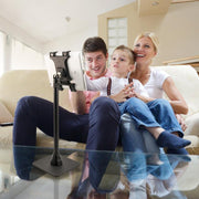 A man, woman, and young boy sit on a couch in a cozy living room, smiling as they look at a tablet secured in the Slim-Grip® Tablet Holder with Height-Adjustable Desk Stand placed in front of them.