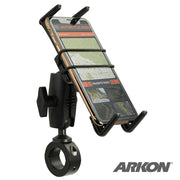 A Slim-Grip® Ultra Phone Holder with Motorcycle Handlebar Mount and 2.75 Shaft in black secures a smartphone on the handlebars, displaying navigation. Adjustable arms and a rubber strap grip the phone, with the Arkon logo visible in the corner.