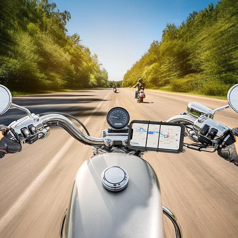 Point-of-view shot from a motorcycle rider on a sunny road, with the Slim-Grip® Ultra Premium Aluminum Motorcycle Handlebar Smartphone Mount visible on the handlebars. Trees line both sides and other motorcyclists are seen ahead in the distance.