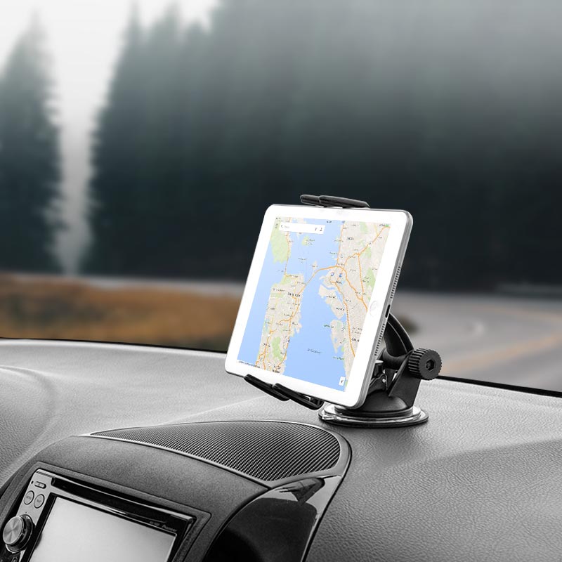 A Slim-Grip® Ultra Windshield or Dash Phone Car Mount securely holds an iPad on the car dashboard as it drives a winding road, with trees and fog visible through the windshield.
