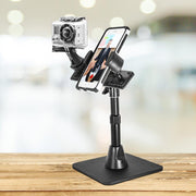 The TW Broadcaster Desk Stand for GoPro and RoadVise® Phone Holder is mounted side by side on a wooden table, perfect for content creators live streaming or filming videos with a blurred indoor background.